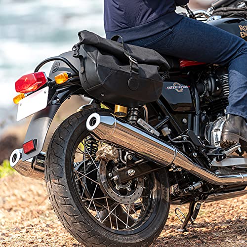 Motorcycle rear view with a black saddlebag, chrome exhaust, and rider in jeans parked on dirt road by the coast